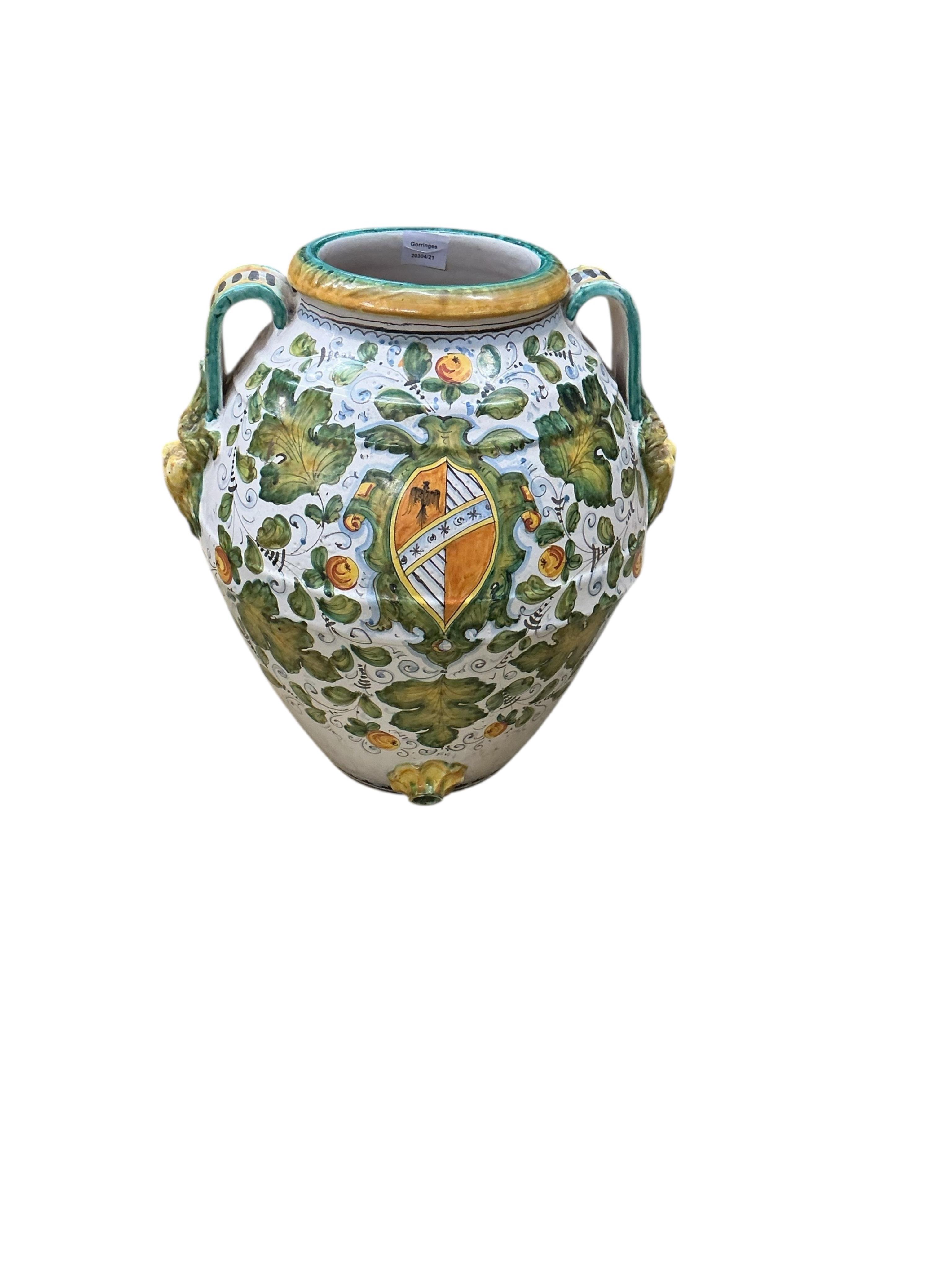 A large Italian Maiolica wine jar with spigot hole, twin handles with grotesque masks, all-over decorated with fruiting foliage and a central armorial cartouche, height 48cm